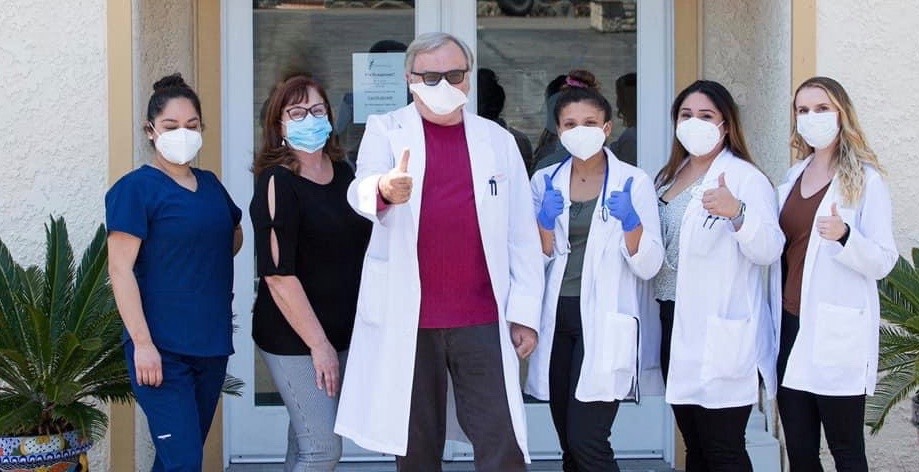 Group of medical providers in lab coats and wearing masks giving thumbs up