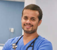 Male GI physician in scrubs with stethoscope smiling in headshot