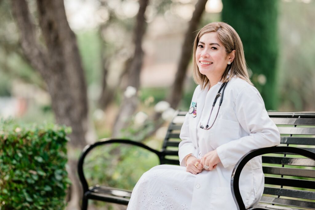 Female nurse practitioner in lab coat sitting on park bench outside
